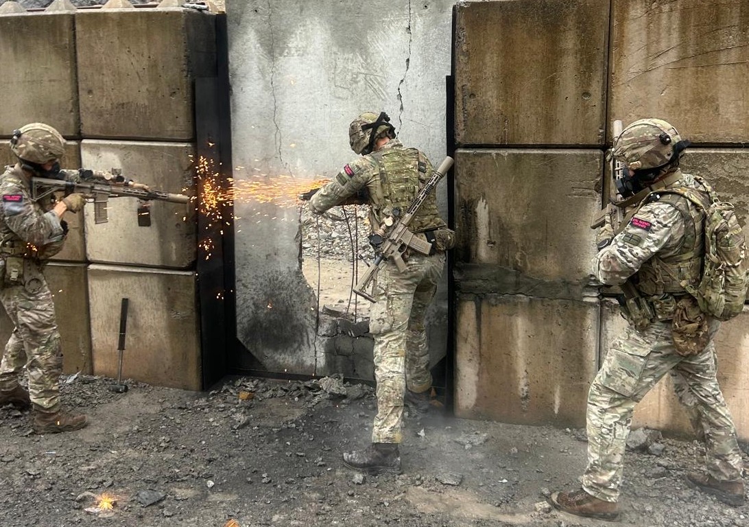 Operators stacked on a concrete wall as a breach charge sparks